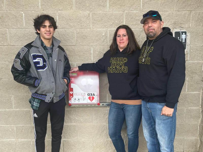 From left: Dylan's parents, Gus and Lisa Dorrell, and brother, Jake Dorrell, with the AED that was placed in the park where Dylan collapsed. (Photo courtesy of the Dorrell family)